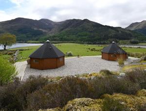 two wooden huts in a field with mountains in the background at Leven View Lodges - Callart in Fort William