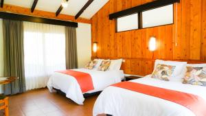 two beds in a room with wooden walls and windows at Hotel de Montaña Suria in San Gerardo de Dota