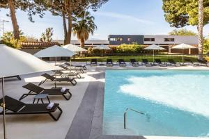 - une piscine avec des chaises et des parasols à côté d'un bâtiment dans l'établissement Holiday Inn Perpignan, an IHG Hotel, à Perpignan