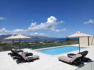 einen Pool mit Stühlen und Sonnenschirmen sowie das Meer in der Unterkunft Villa Kafkales Maleme - Heated Pool in Maleme