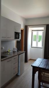 uma cozinha com armários brancos, uma mesa e uma janela em Quinta do Oratório Agroturismo em Óbidos