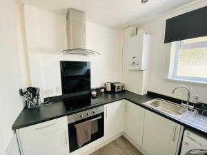 cocina con armarios blancos y encimera negra en Emerald Properties UK 4 bedrooms - Swansea City Centre, close to beaches!, en Swansea