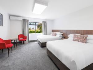 a hotel room with two beds and a desk and chairs at JetPark Hamilton Airport New Zealand in Hamilton +44 photos