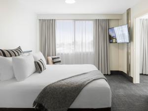 a hotel room with a large white bed and a tv at JetPark Auckland Airport Hotel in Auckland