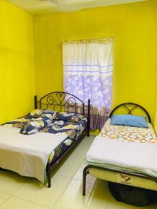 two beds in a room with yellow walls and a window at Homestay Zalida C Musleem in Kampong Alor Gajah