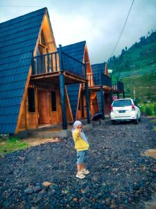 un jeune enfant debout devant une maison dans l'établissement Cabin LEHA LEHE SYARIAH Dieng, à Diyeng