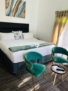 a bedroom with a bed and two green chairs at St Eve Lodge & Spa in Bloemfontein