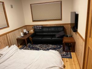 a living room with a black leather couch and a television at 離れの宿　かぶろの庭 in Matsukawa