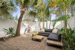 a patio with a couch and a table and palm trees at Vibes At Five Noosa in Noosaville