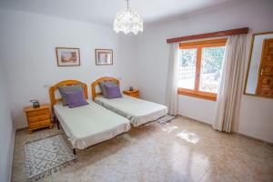 two beds in a bedroom with a window and a chandelier at Casa de Campo Cala Bassa in Sant Josep de sa Talaia