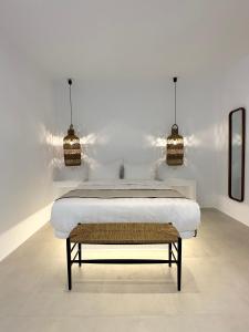 Quattro Venti Suites Mykonos في تورلوس: غرفة نوم بيضاء بها سرير وعلاقتين انارة