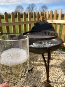 een persoon met een glas wijn naast een grill bij Marsh Farm Glamping Shepherd Hut in Langport