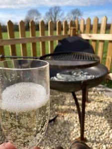 a person holding a glass of wine next to a grill at Marsh Farm Glamping Shepherd Hut in Langport