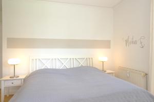 a white bedroom with a white bed with two lamps at Dünenblick Wohnung 22 in Boltenhagen