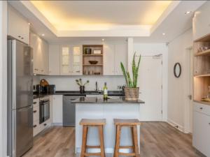 eine Küche mit weißen Schränken und einer Insel mit zwei Hockern in der Unterkunft Edgy On Bree in Kapstadt