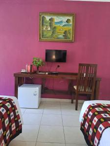 Habitación con escritorio y TV en una pared rosa. en Lovina Beach Hotel, en Lovina