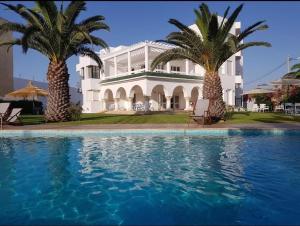 une grande maison blanche avec des palmiers et une piscine dans l'établissement Dar Oguz, à Ḩammām al Ghazzāz