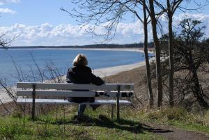 Eine Frau, die auf einer Bank sitzt und den Strand ansieht. in der Unterkunft Strandhaus Lobbe - Fewo 45499 in Lobbe