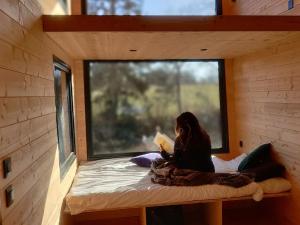 a woman sitting on a bed reading a book in a tiny house at Tiny House MOOSE HOME Les Chaumes in Les Ancizes-Comps