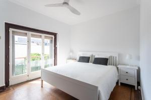 a white bedroom with a large bed and a window at Villa Jacarandá in Cascais