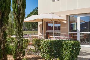 une table avec un parasol devant un bâtiment dans l'établissement Kyriad Direct Mont De Marsan - St Avit, à Saint-Avit