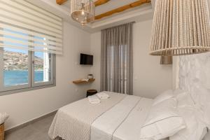 a white bedroom with a bed and a window at Porto Dema Luxury Suites in Schinoussa