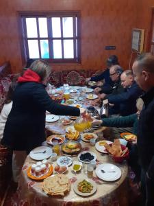 un grupo de personas sentadas alrededor de una mesa comiendo comida en Kasbah La Famille Berbère en Boumalne
