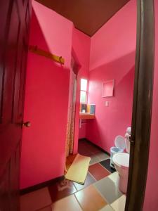 a bathroom with a pink wall and a toilet at Hotel Sunset Rooms in Tortuguero