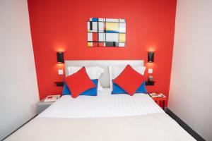 czerwona sypialnia z białym łóżkiem z czerwonymi i niebieskimi poduszkami w obiekcie Hôtel Du Mont Dore Batignolles w Paryżu