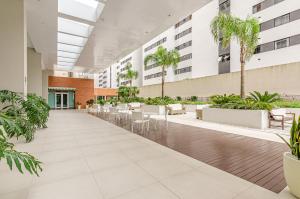 um átrio vazio com mesas, cadeiras e palmeiras em Lifespace Curitiba - Duplex Incrível, 2 Quartos, varanda, 2 garagens Batel em Curitiba
