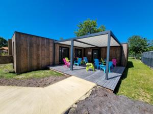 une maison dotée d'une terrasse avec des chaises colorées. dans l'établissement La cabane 27 ~ Chalet cosy au bord du lac de Peyre, à Labouheyre