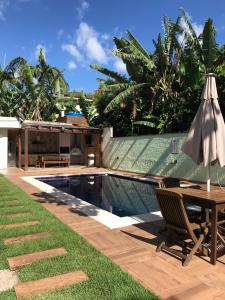 - une terrasse avec une table et un parasol à côté de la piscine dans l'établissement Casa de Condomínio em Maresias - Pertinho da praia, à Maresias