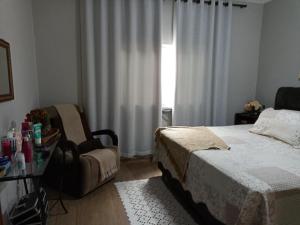 a bedroom with a bed and a chair and a window at Casa da Nice in Guaratinguetá