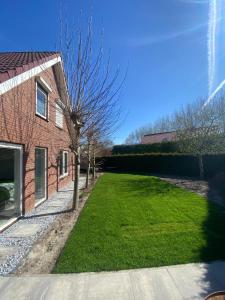 um quintal ao lado de uma casa de tijolos com um relvado verde em Luxurious Family Villa with swimmingpool big garden and jacuzzi em Zeewolde