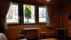Pokój z 3 oknami, stołem i stołkami w obiekcie Cottage Morino Nakamatachi w mieście Furano