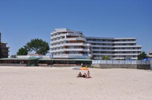 two people sitting under an umbrella on the beach at Hotel Lido in Mamaia