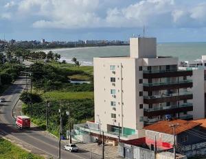 a tall white building next to a road next to the ocean at Vela e Mar in João Pessoa