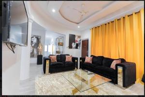 una sala de estar con 2 sofás negros y cortinas amarillas. en Cozy homes Accra,Ghana en Owuraman