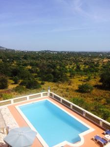 a swimming pool with an umbrella and chairs and an ocean at Quinta do Atlantico in Santa Bárbara de Nexe