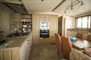a kitchen with wooden cabinets and a table with chairs at Beautiful Caravan With Stunning Sea Views At Haven Hopton Ref 80001h in Great Yarmouth