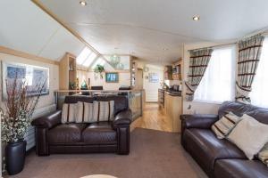 a living room with two leather couches and a kitchen at Luxury Caravan For Hire At Hopton Holiday Park With Full Sea Views Ref 80010h in Great Yarmouth
