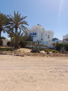 a beach with palm trees and a white building at Dar Lagune Djerba in Al Ḩaddādah