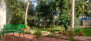 a green bench sitting in a garden with palm trees at Coralshelters Kochadai in Madurai
