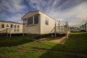 a small yellow house with a porch on a lawn at Lovely Caravan With Decking At Manor Park Nearby Hunstanton Beach Ref 23017t in Hunstanton