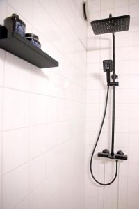 a shower in a white tiled bathroom with a black shower head at Kaunis ydinkeskustan huoneisto in Tampere