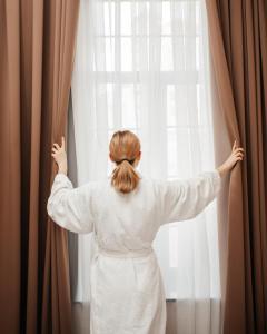 Una donna con un vestito bianco che guarda fuori da una finestra di OLF Hotel a Baku