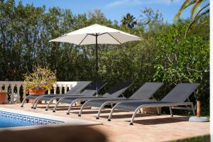 uma fila de espreguiçadeiras com um guarda-sol ao lado de uma piscina em Casa Luzerna em Carvoeiro