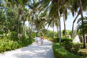twee mensen lopen over een pad met palmbomen bij Centara Ras Fushi Resort & Spa Maldives in North Male Atoll
