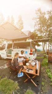 Ein Mann und eine Frau sitzen an einem Tisch vor einem Wohnwagen. in der Unterkunft Campervan Bali Rental in Dalung