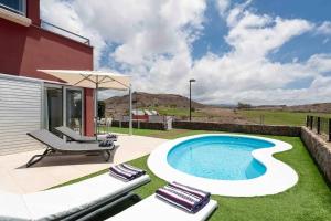 a backyard with a swimming pool and chairs and an umbrella at Sea View Villa Vista Golf in Salobre